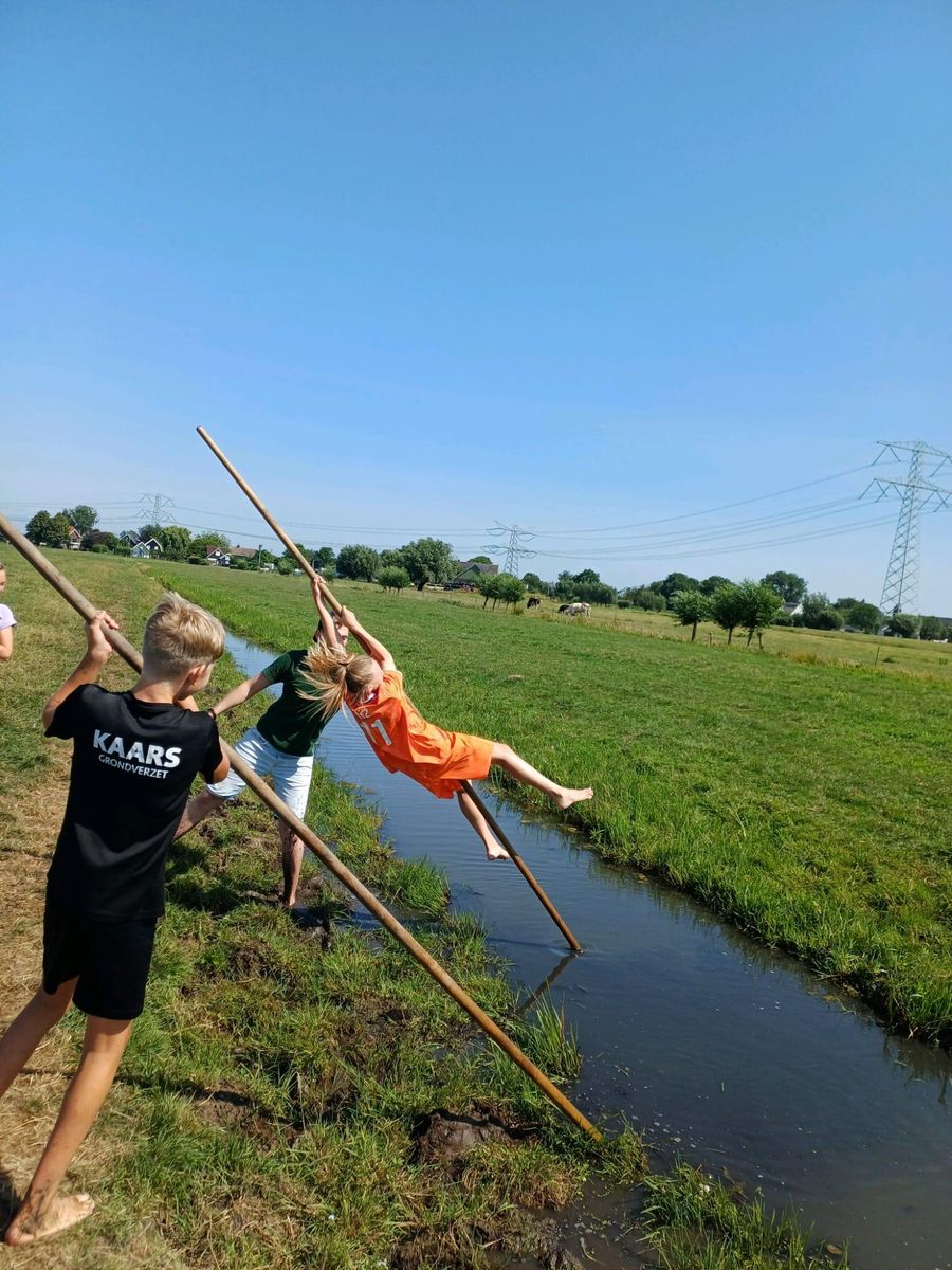 Deelnemer met een polsstok boven de sloot