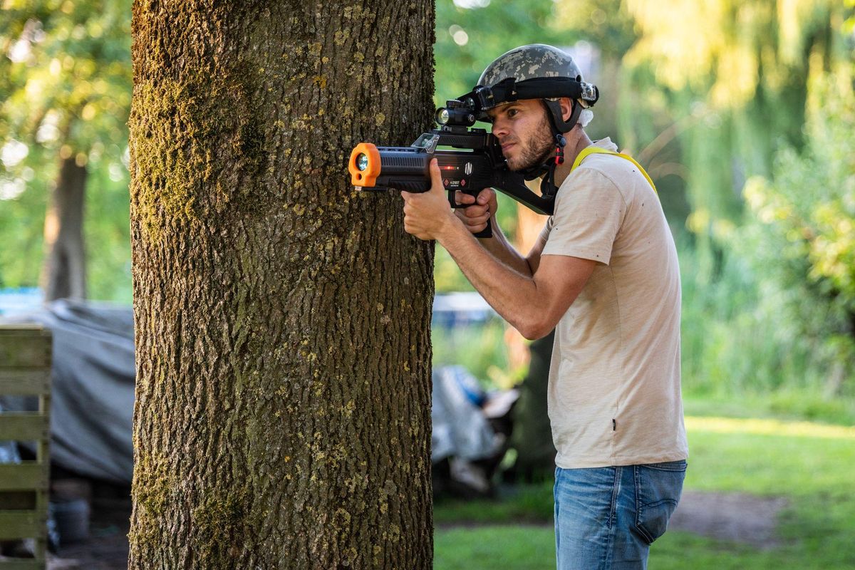 Volwassen speler in dekking achter een boom tijdens het outdoor lasergamen